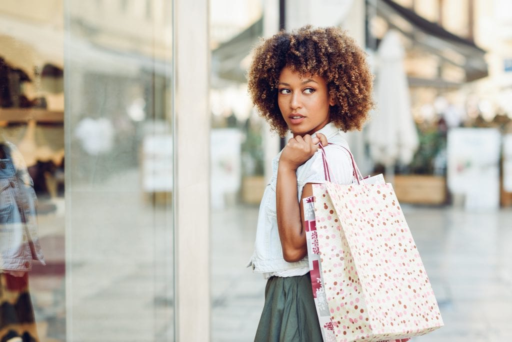 Young black woman in front of a shop window in a shopping street. African girl with afro hairstyle wearing casual clothes.