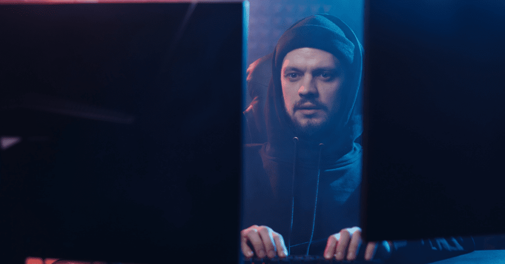 sketchy man behind two monitors wearing a black beanie