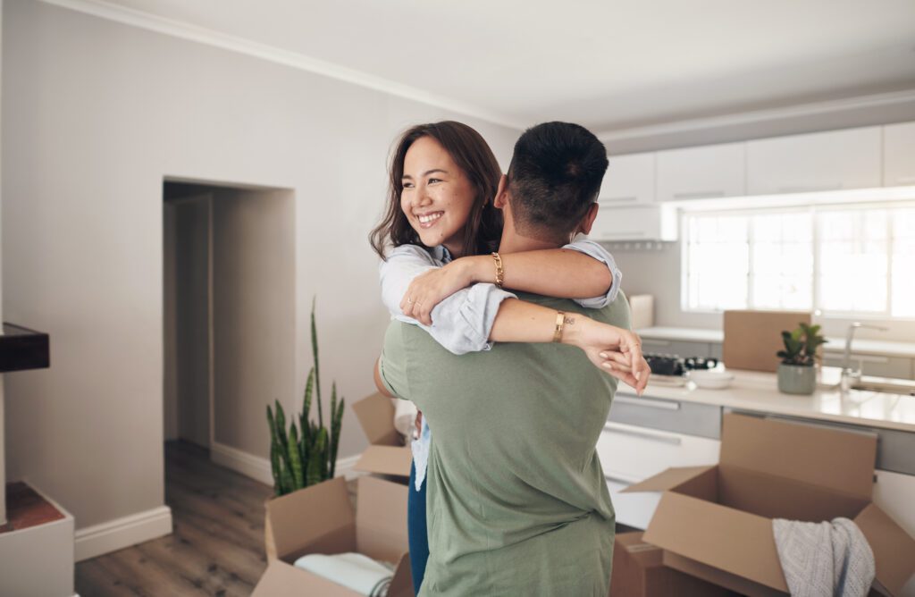 Property, happy couple moving into their new home and boxes in living room. Happiness or smiling, mortgage or homeowners and people hugging celebrating with their new house or apartment together.